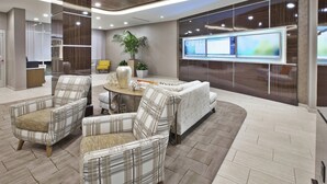 A modern lobby with a seating area featuring plaid armchairs and a sofa, a large potted plant, and a wall-mounted TV. - SpringHill Suites by Marriott Chattanooga North/Ooltewah (Ooltewah)