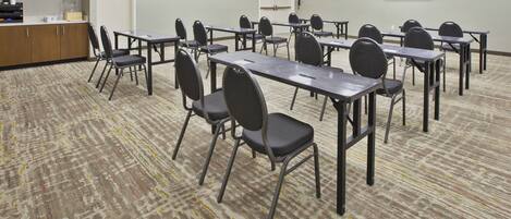 A conference room with multiple tables and chairs, a flat-screen TV on the wall, and a carpeted floor.