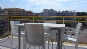 A balcony with a table and chairs, overlooking a cityscape with buildings and a clear sky. - Rentalmar Navarra (Salou)