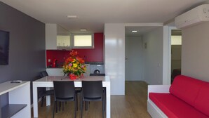 A modern kitchen with white cabinets, a red backsplash, and a dining area with a white table and black chairs. - Rentalmar Navarra (Salou)