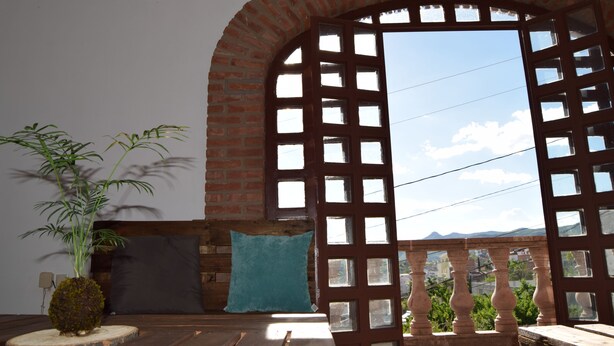 A room with a wooden bed, a blue pillow, a potted plant, and a view through a lattice window. - Casa Palmas (Guanajuato)