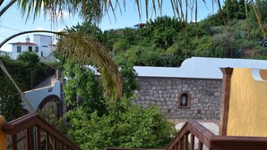 A staircase leading to a stone building with a white roof, surrounded by greenery and a view of a hill with houses. - Casa Palmas (Guanajuato)