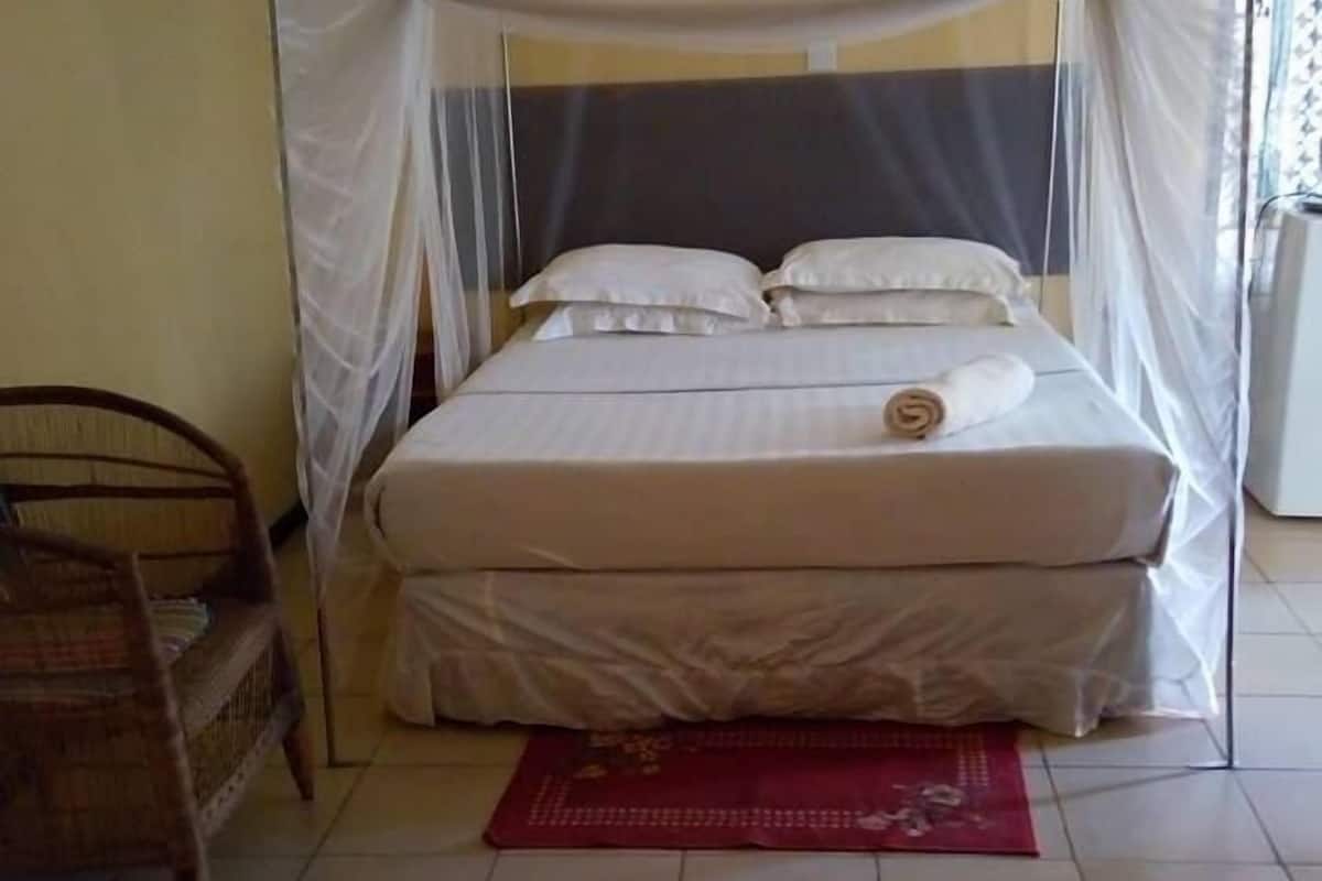 A bed with a canopy, a red mat, and a wooden chair.