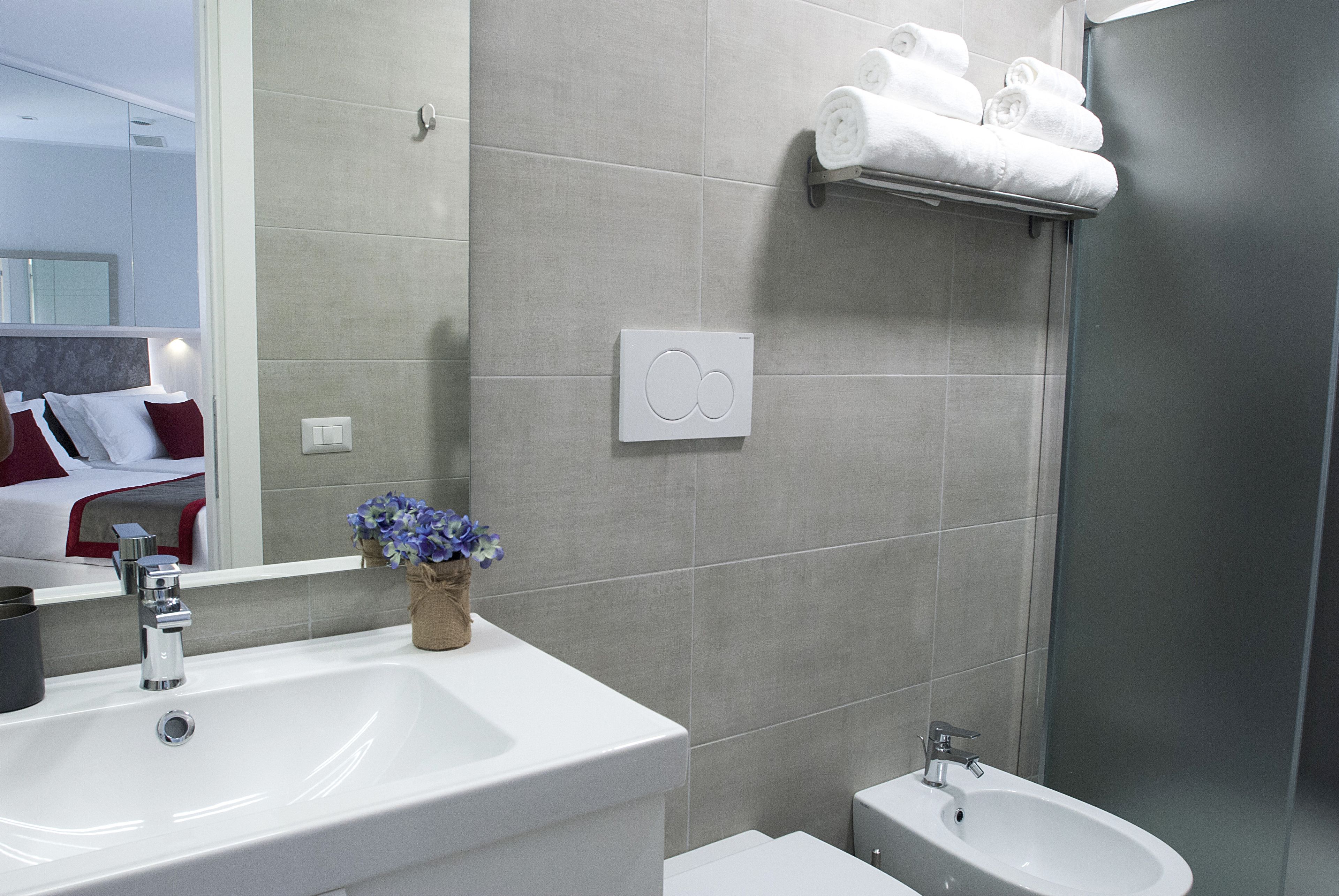 A modern bathroom with a large mirror, a sink, a bidet, and a towel rack.
