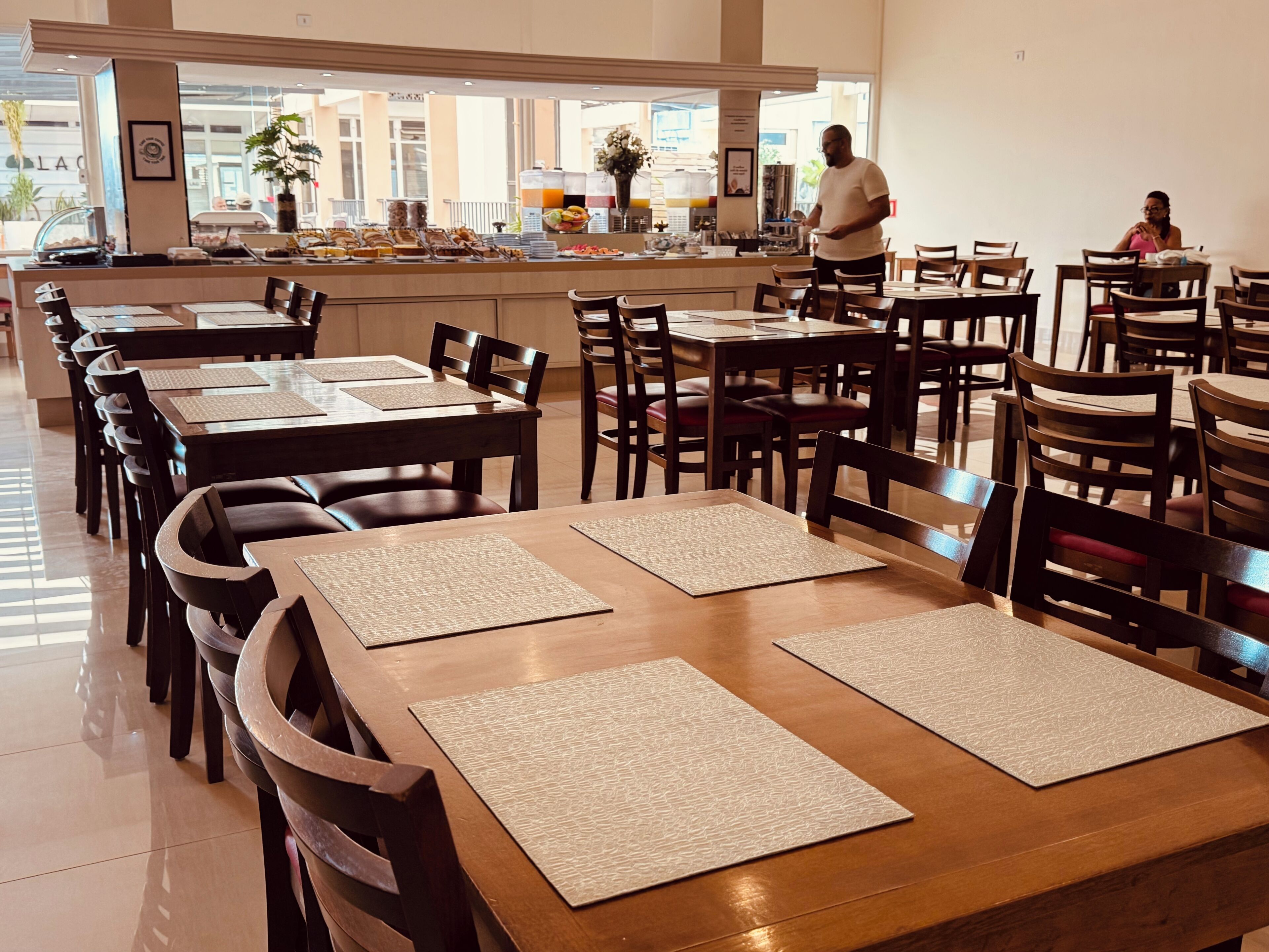 A restaurant with multiple tables and chairs, a buffet area, and a person standing near the counter.