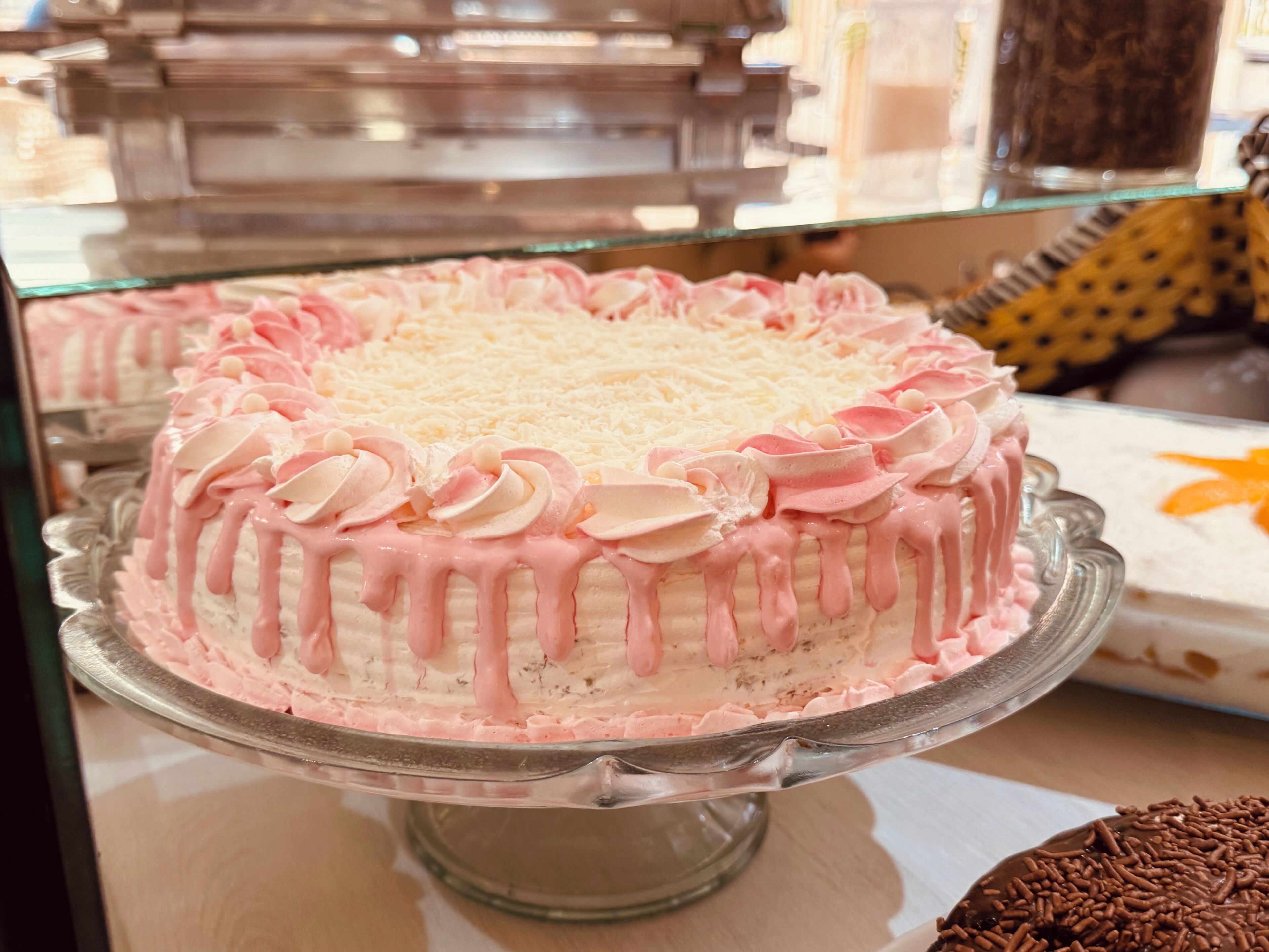 Un pastel con cobertura rosa y decoraciones blancas sobre un expositor de vidrio.