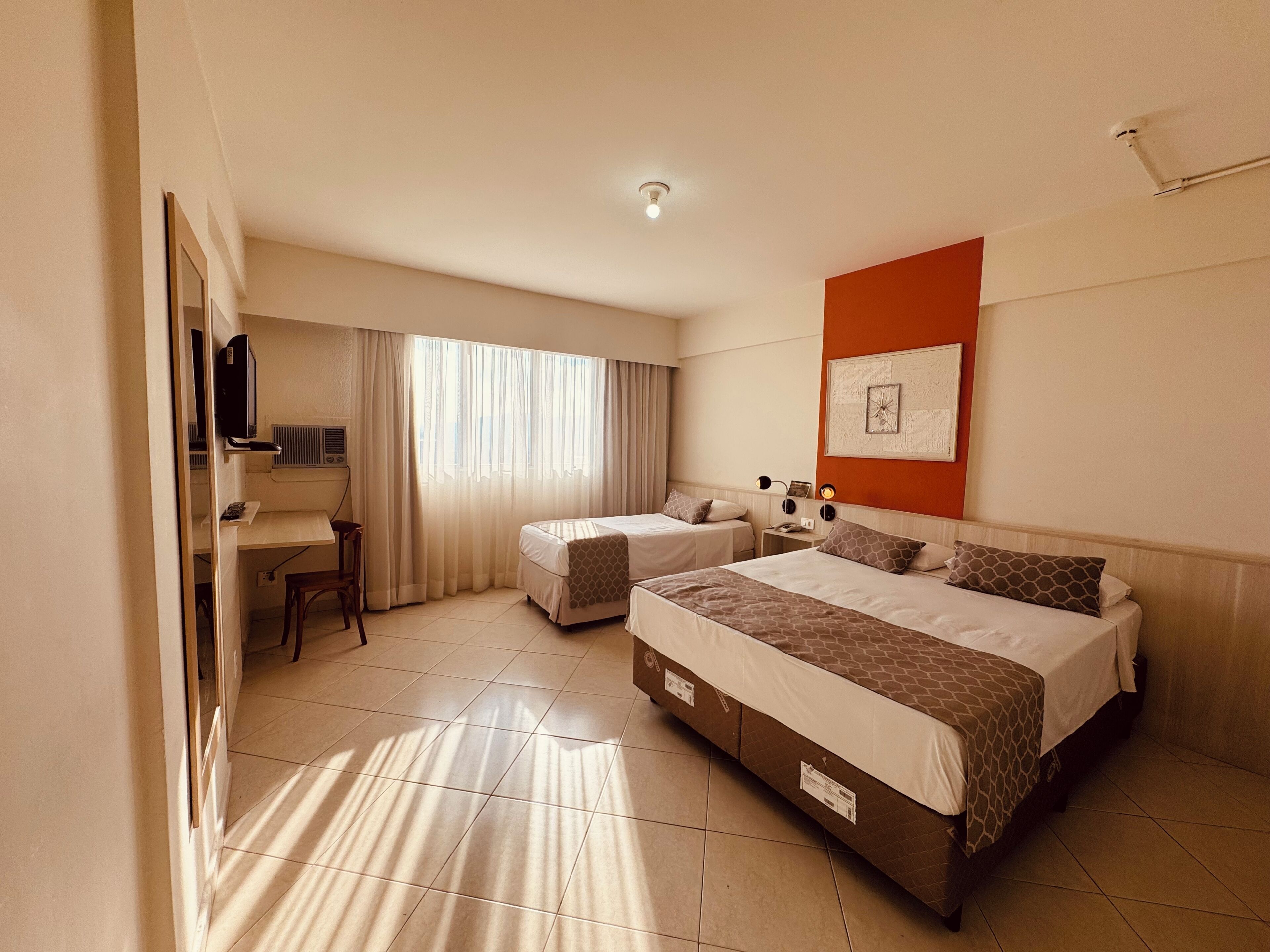 Habitación de hotel con dos camas, un escritorio, una silla, un televisor y una ventana con cortinas.