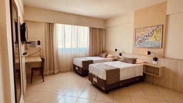 A hotel room with two beds, a desk, a chair, and a large window with curtains.