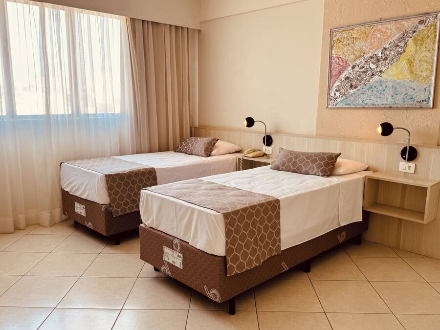 Habitación de hotel con dos camas, una mesita de noche con lámpara, teléfono y un mapa colgado en la pared.
