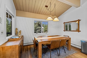 A dining area with a wooden table and chairs, a chandelier, and a large mirror on the wall.