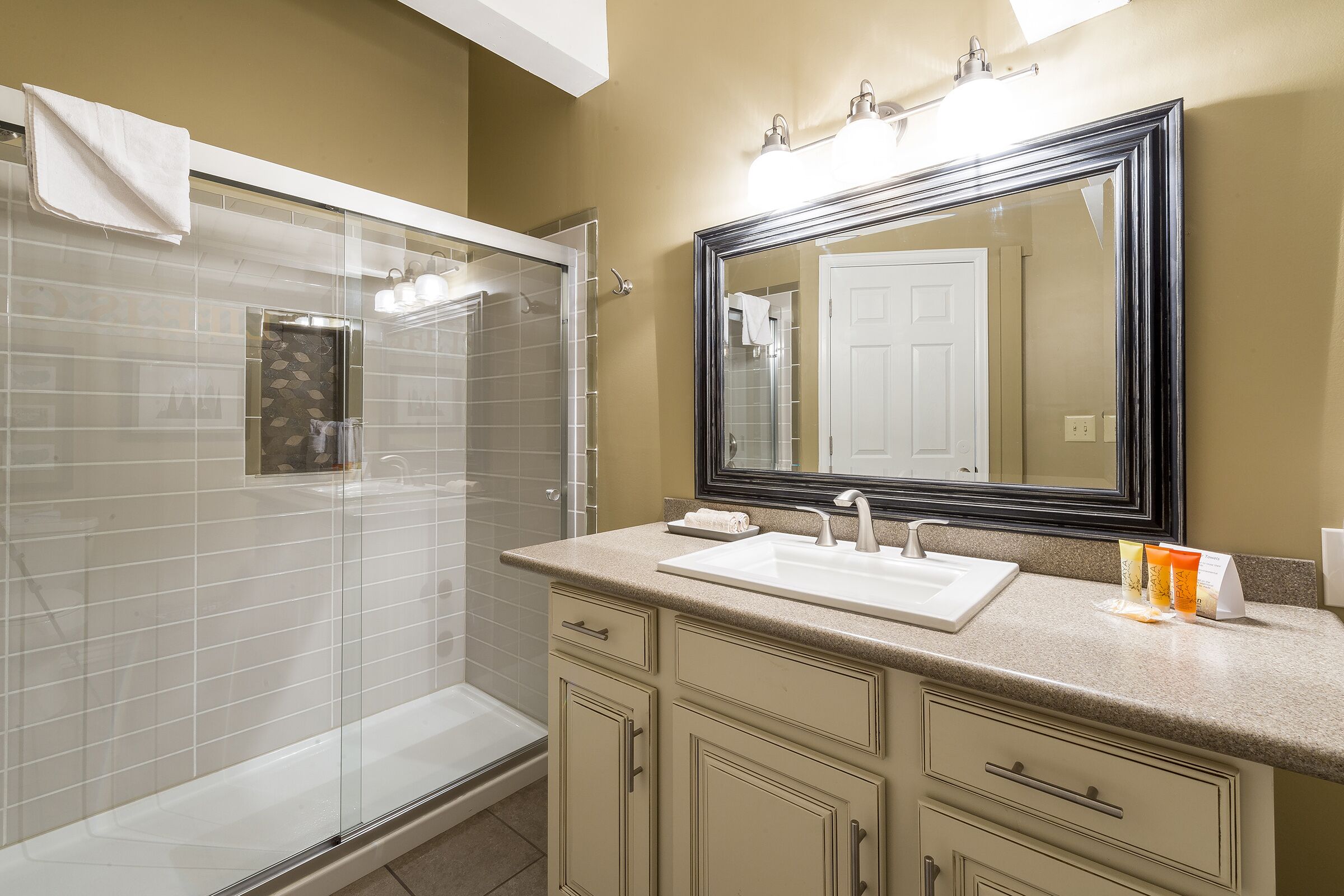 Une salle de bain avec une douche à parois de verre, un lavabo avec un miroir au-dessus et des meubles de couleur beige.