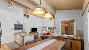 Une cuisine moderne avec une table à manger en bois, des luminaires suspendus et une vue sur l’extérieur.
