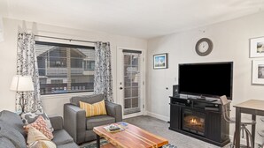 A living room with a sofa, coffee table, fireplace, TV, and curtains. - First Tracks 3301 2 Bedroom Condo by RedAwning (Steamboat Springs)