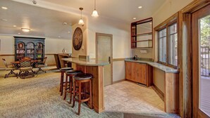 A kitchen with a bar area, wooden cabinets, and a large clock on the wall. - Phoenix 118A - 3 Br Condo (Steamboat Springs)