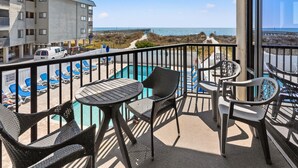 A balcony with a pool, lounge chairs, and a view of the beach and ocean. - Sedgefield 102 by RedAwning (North Myrtle Beach)