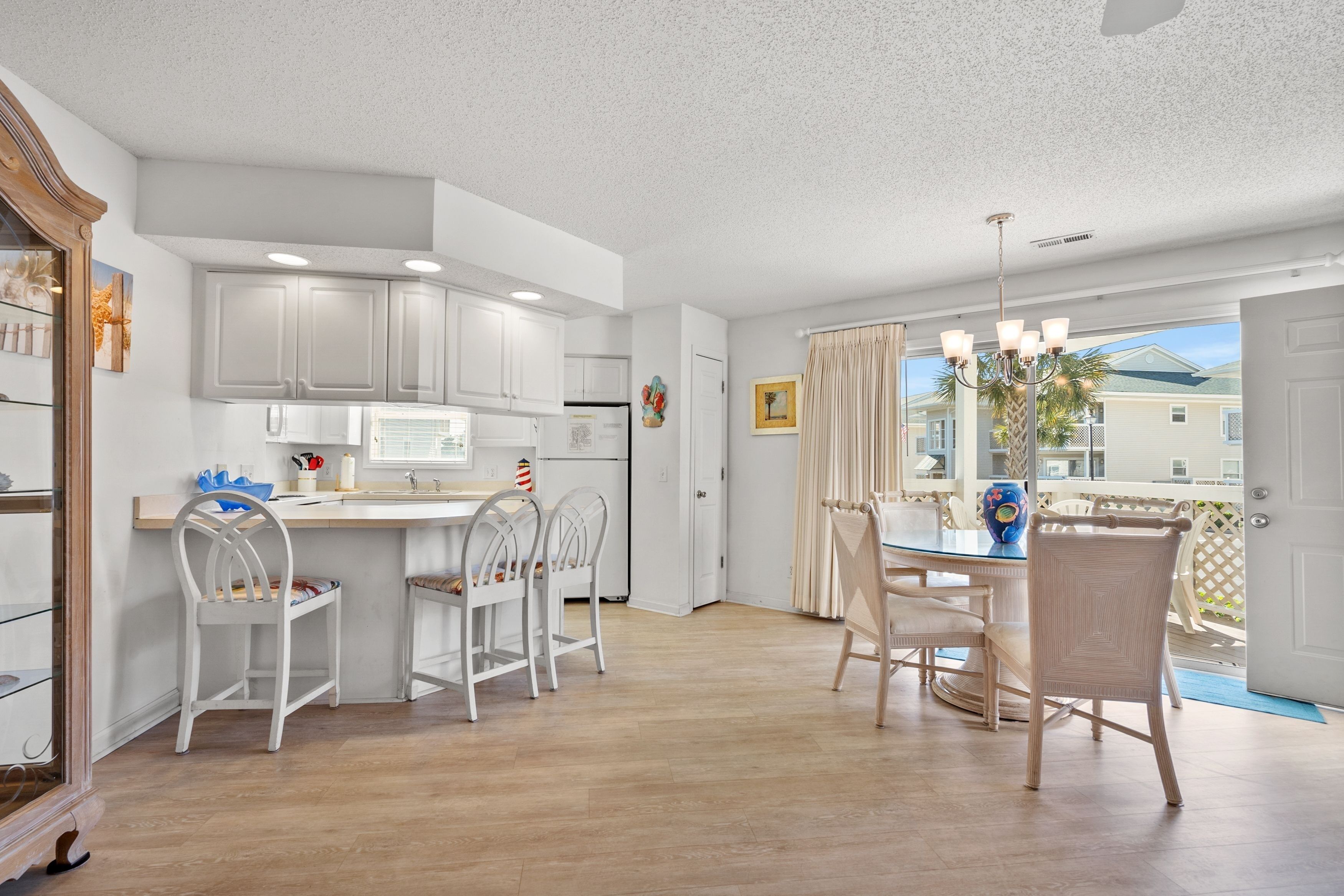 A modern kitchen with white cabinets, a dining area with white chairs, and a view of the outside.