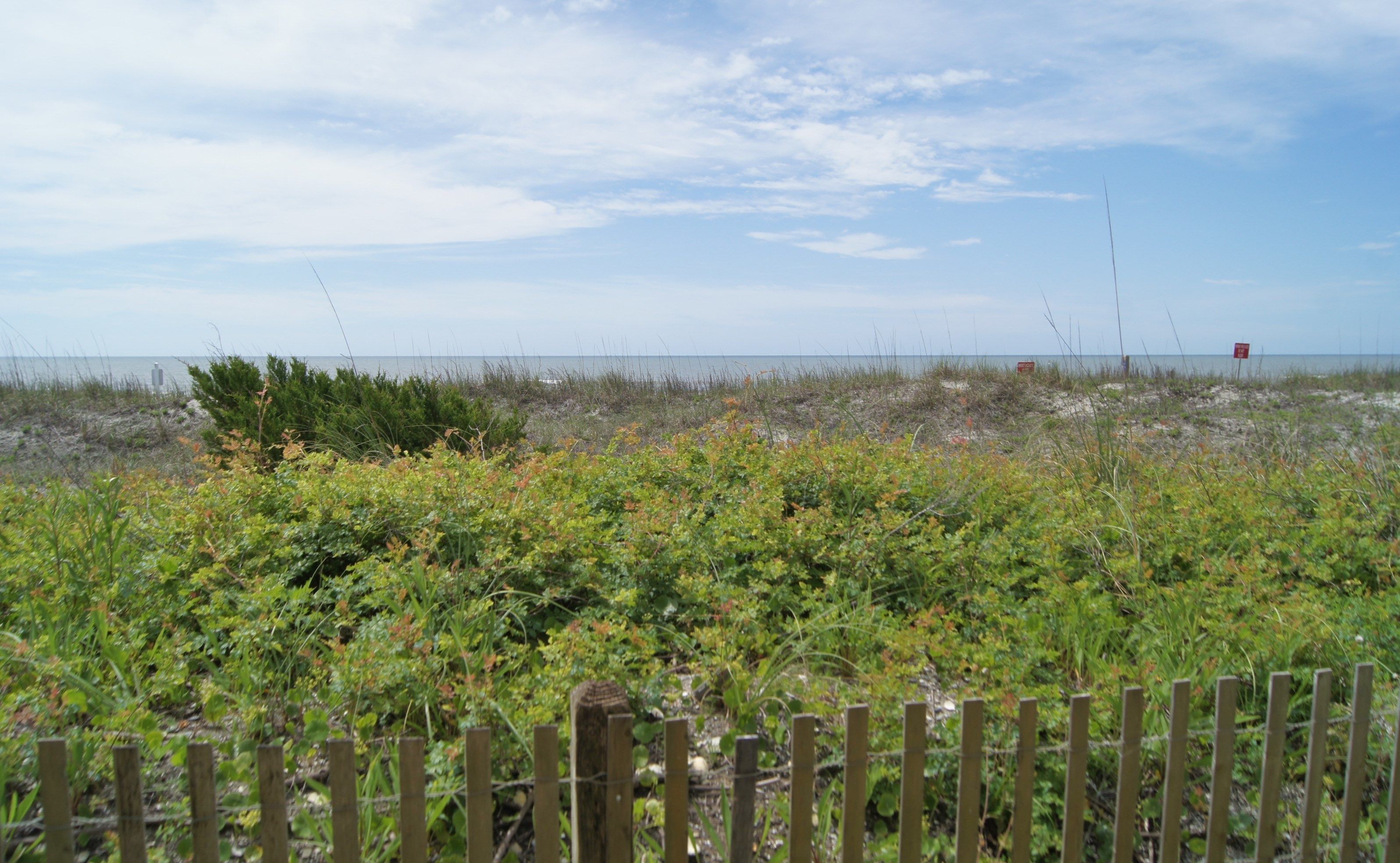 A beach with a wooden fence in the foreground and a red sign in the distance.