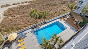 A pool area with a view of the beach, palm trees, and a building with balconies. - Shoreham Towers 5C by RedAwning (North Myrtle Beach)