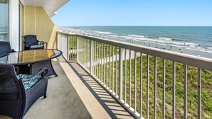 A balcony with a glass table and chairs, overlooking a beach with a pier in the distance. - Sunrise Pointe 4F by RedAwning (North Myrtle Beach)