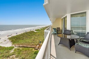 Un balcon avec vue sur la plage, une table et des chaises, et une porte vitrée.
