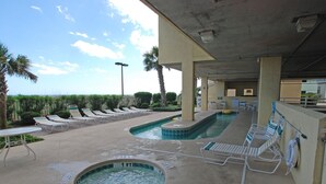A pool area with lounge chairs and a hot tub, surrounded by palm trees and a view of the ocean. - Sunrise Pointe 4F by RedAwning (North Myrtle Beach)