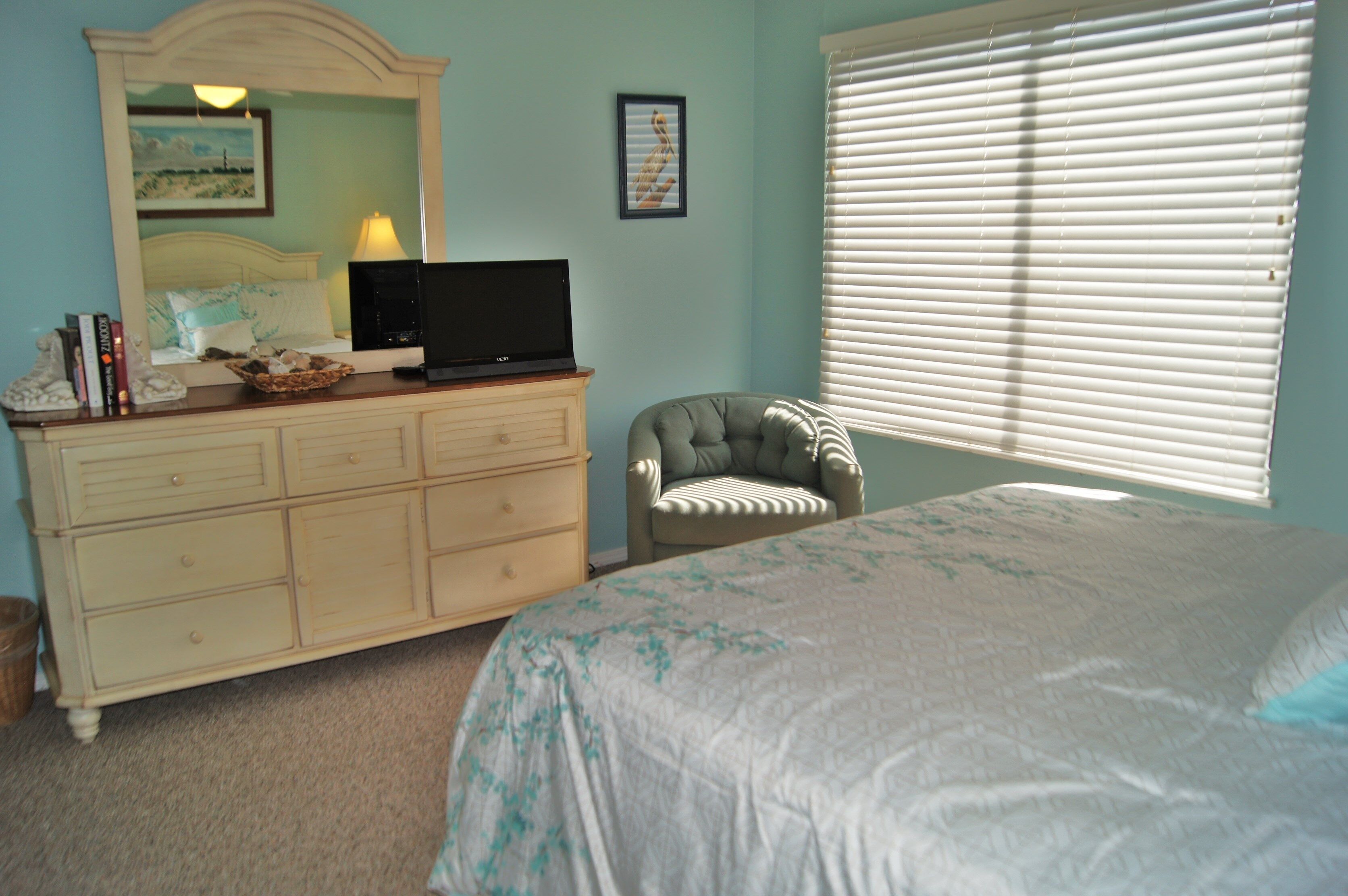 A bedroom with a bed, dresser, chair, and a window with blinds.