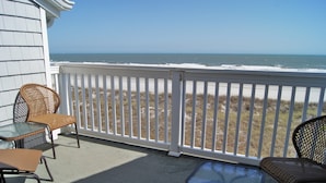 A balcony with wicker chairs and a glass table, overlooking a beach with a white fence and ocean view. - Sea Cloisters 305C by RedAwning (North Myrtle Beach)