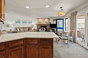 A modern kitchen with a large island, dining area with chairs, and a fireplace. - Tilghman Lakes B3 by RedAwning (North Myrtle Beach)