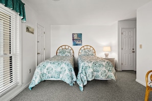 A bedroom with two single beds, a nightstand with a lamp, and a door with a window on the left. - Tilghman Lakes B3 by RedAwning (North Myrtle Beach)