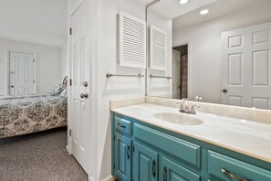 A bedroom with a bed, a bathroom with a sink and mirror, and a door leading to another room. - Tilghman Lakes B3 by RedAwning (North Myrtle Beach)