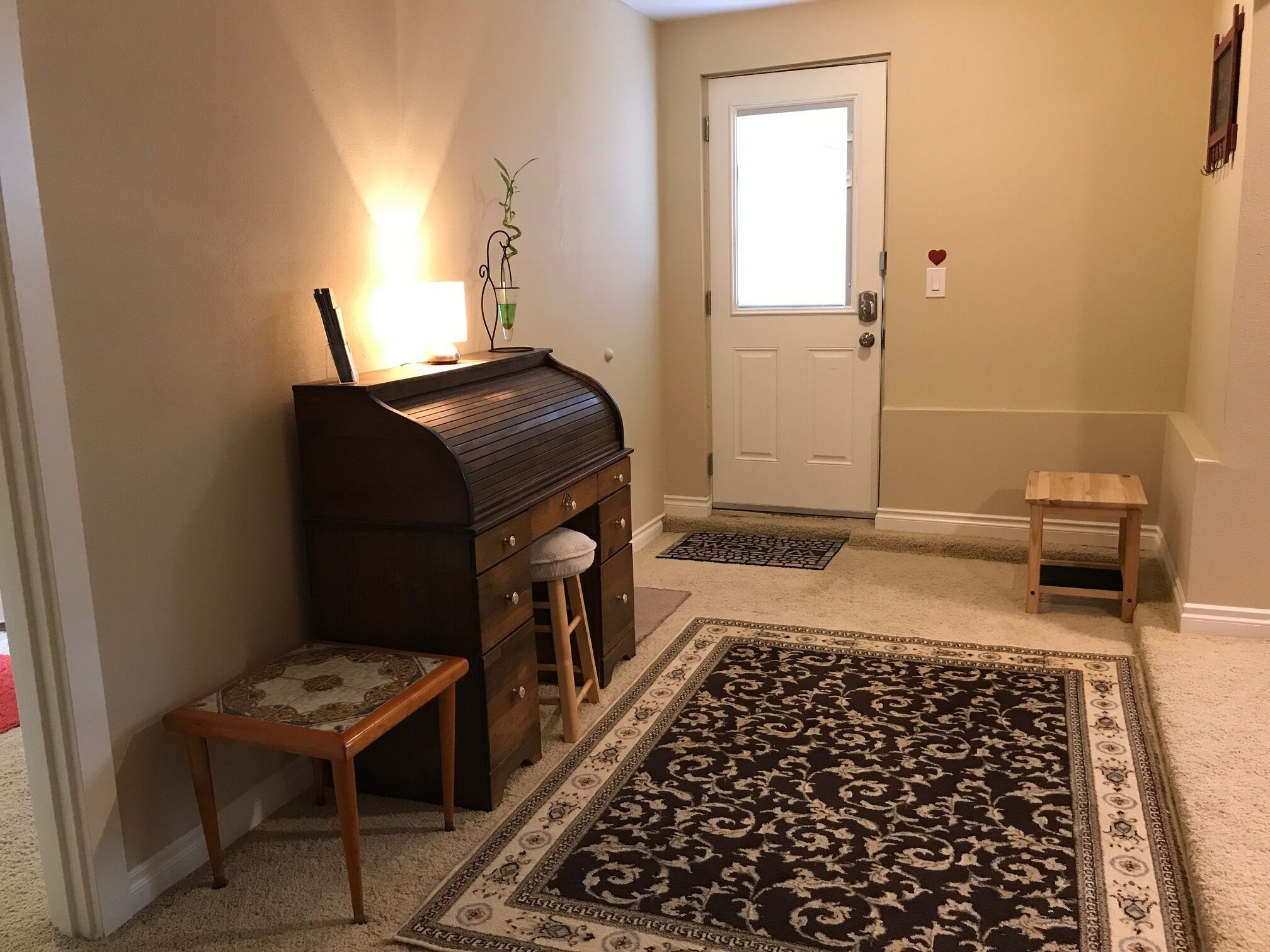 Un piano dans un couloir, avec un tapis, une porte et un petit tabouret.