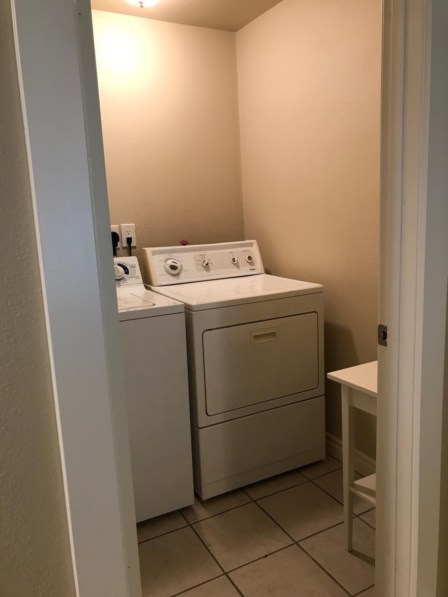 Un cuarto de lavandería con lavadora y secadora, una pequeña mesa y un enchufe de pared.