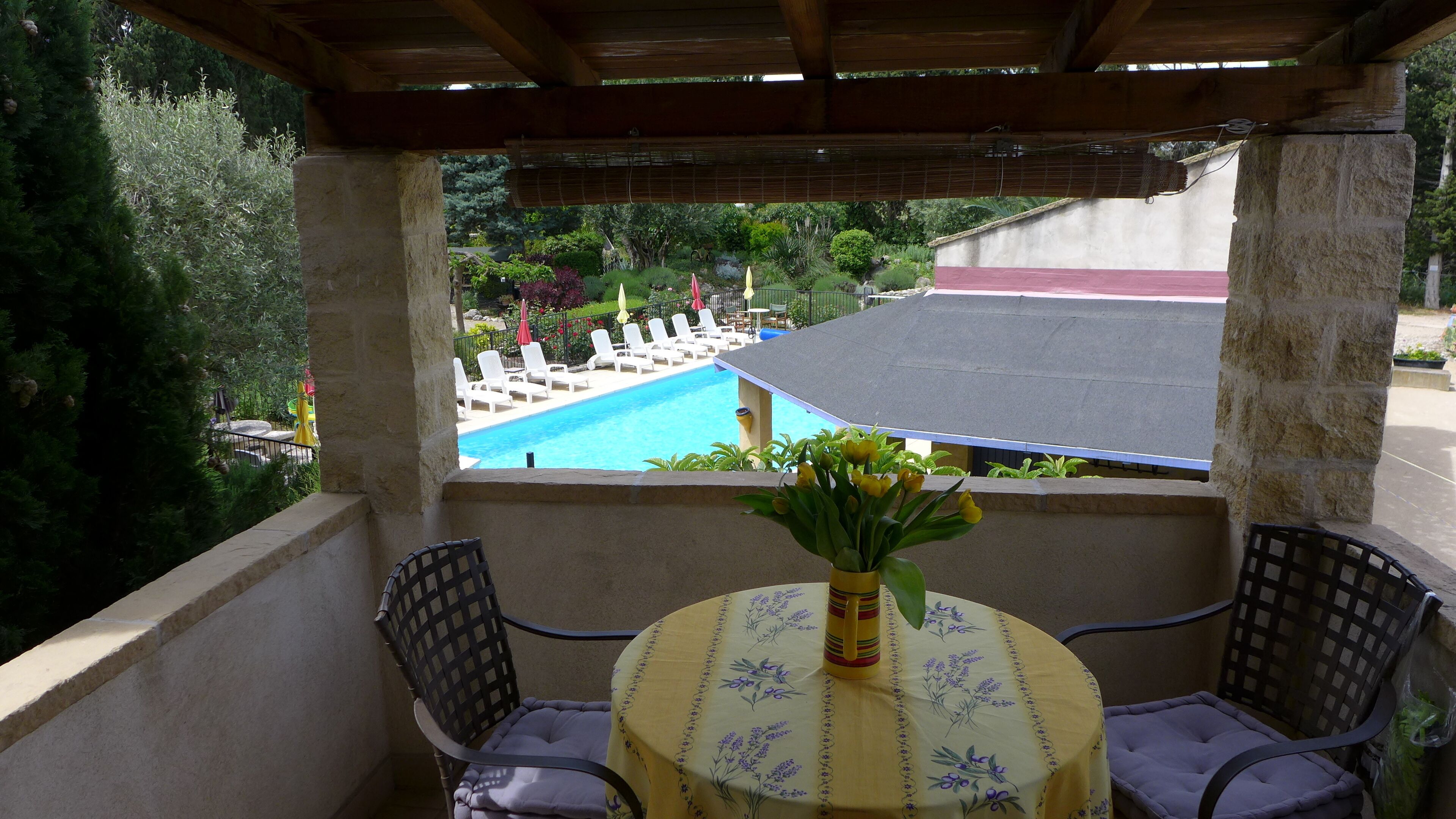 A balcony with a view of a swimming pool, a table with a floral tablecloth, and two chairs.