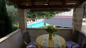 Un balcon donnant sur une piscine, une table recouverte d’une nappe à motifs floraux et deux chaises.