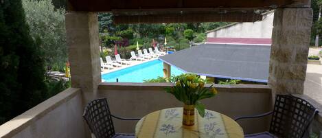 A balcony with a view of a swimming pool, a table with a floral tablecloth, and two chairs.