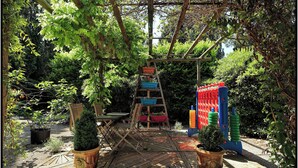 Une terrasse en bois avec une échelle menant à une pergola en bois, entourée de plantes en pot et d’une structure de jeu colorée.