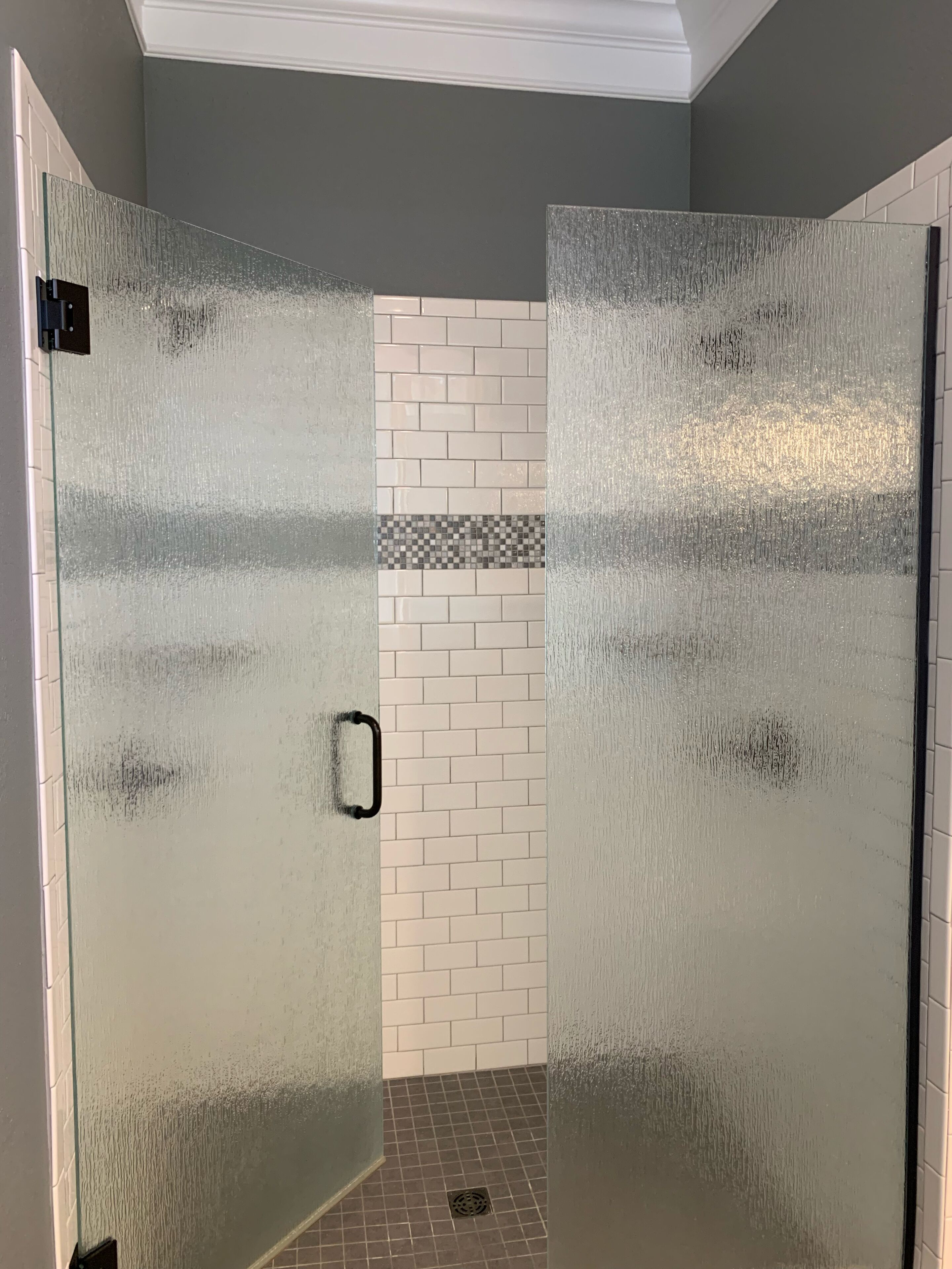 A glass door leading to a shower area with a tiled wall and a drain.