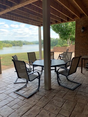 Un patio al aire libre con una mesa y sillas, con vista a un lago y rodeado de árboles.