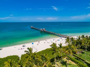 A beach with a long pier extending into the ocean, surrounded by palm trees and a well-maintained lawn. - 1st floor by pool, beach and 3rd St. S coffee shops, restaurants and farmer Mkt (Naples)