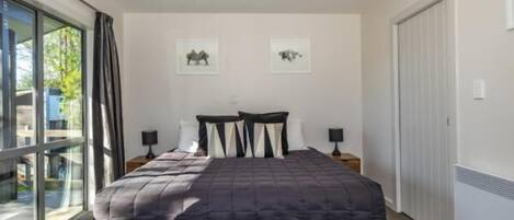 A bedroom with a large bed, two bedside tables, and a sliding glass door to a balcony.