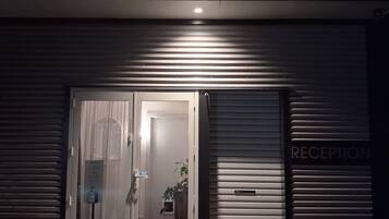 Entrada de um edifício com área de recepção, porta com painel de vidro e tapete de boas-vindas.