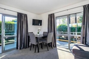 A room with a dining table, chairs, a flat-screen TV, and large sliding glass doors. - Black on Grey Motel (Geraldine)
