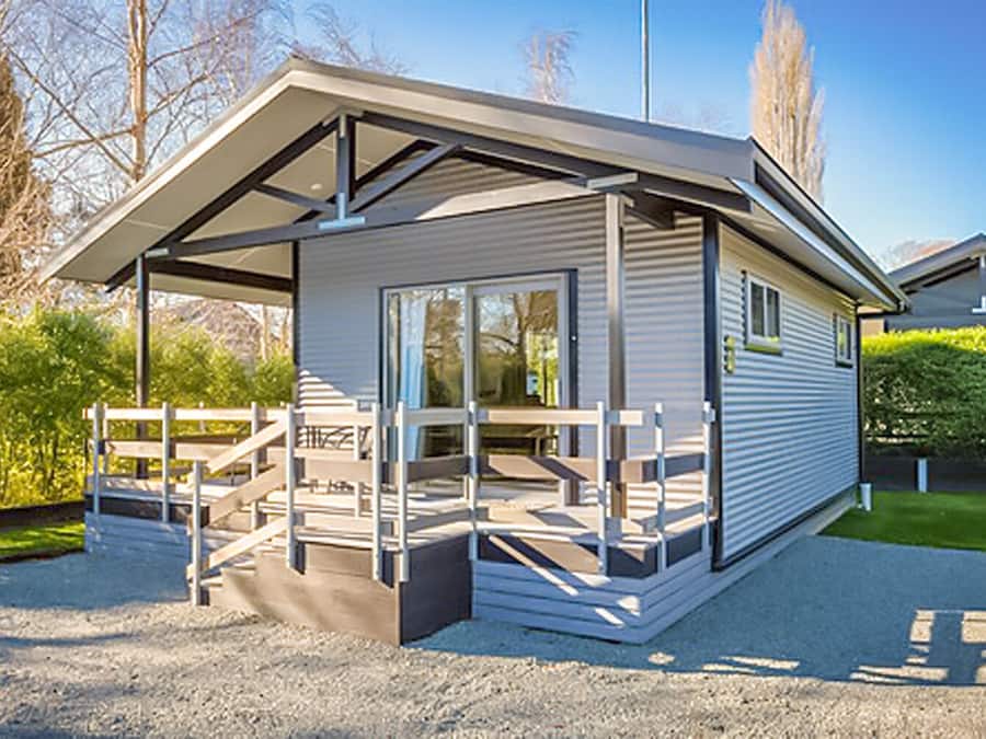 A modern, single-story structure with a covered patio area, large windows, and a gravel driveway.