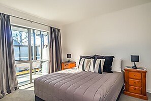 Un dormitorio con una cama grande, dos mesitas de noche, una ventana con cortinas y vistas al exterior.