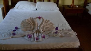 Un lit bien fait, avec des serviettes disposées en éventail et des fleurs violettes sur la couvre-lit.