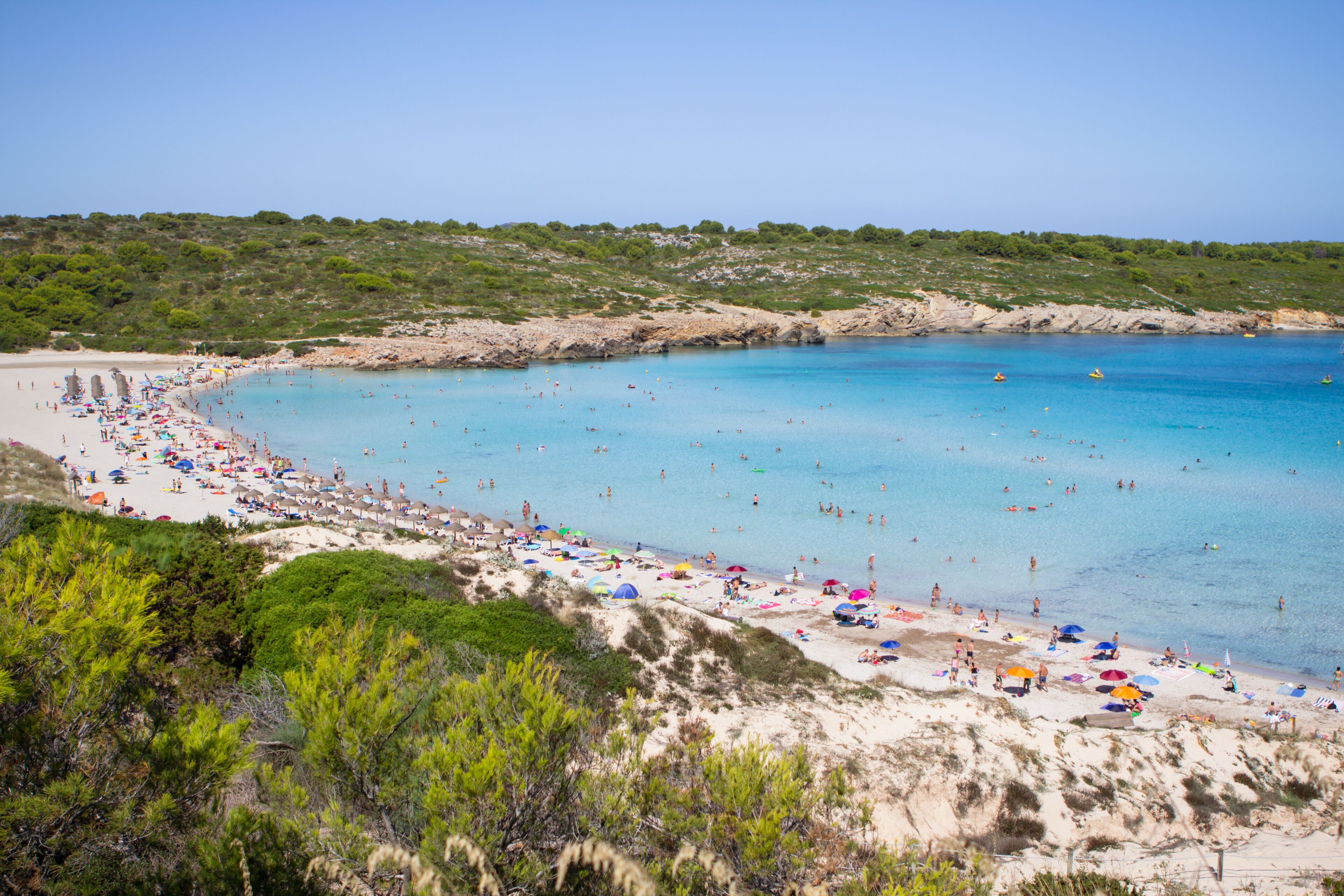 A beach with clear blue water, sandy shores, and numerous colorful umbrellas.