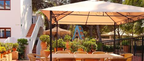 A patio with wicker tables and chairs, a large umbrella, and potted plants.