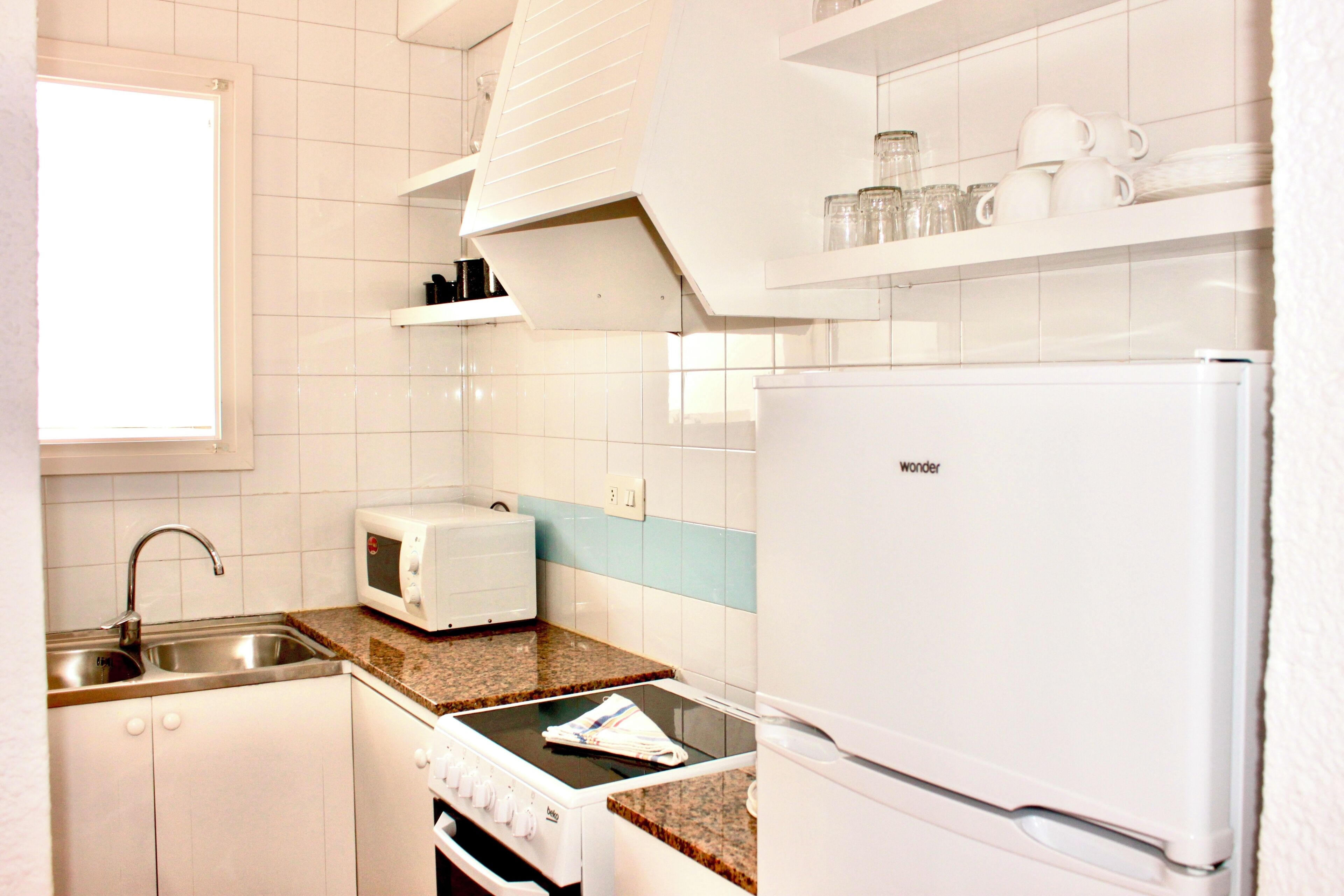 Une cuisine compacte avec des meubles blancs, un four à micro-ondes encastré, une cuisinière et un réfrigérateur.