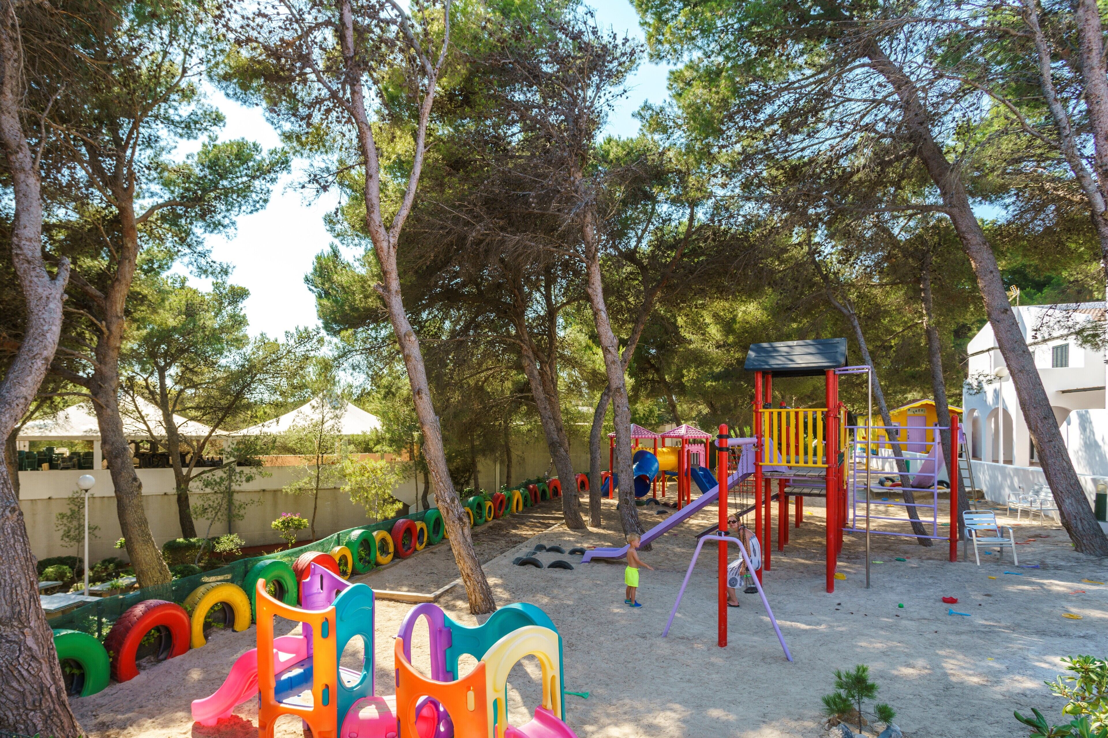 Un terrain de jeux avec des structures colorées et des balançoires faites de pneus, entouré d’arbres.