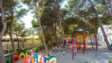 Un terrain de jeux avec des structures colorées et des balançoires faites de pneus, entouré d’arbres.